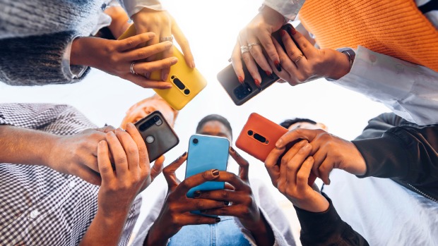 Das Foto ist von unten aufgenommen und zeigt eine Gruppe von Menschen, die im Kreis steht und verschiedenfarbige Handys in den Händen hält. 