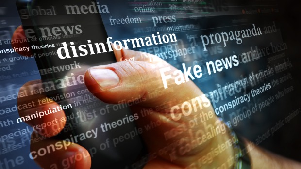 Eine Hand hält ein Handy, davor laufen Schriftzüge, zu lesen sind die Wörter Desinformation, Fake News, Propaganda, Manpulation.