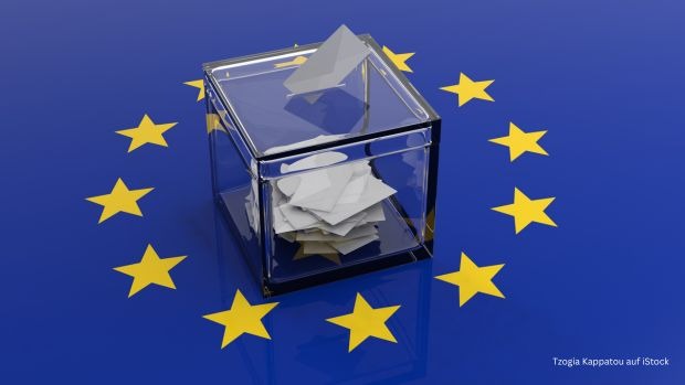 Zu sehen ist der gelbe Sternenkreis der Europaflagge vor blauem Hintergrund, in der Mitte des Kreises steht eine Wahlurne mit Wahlbriefen.